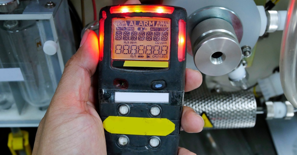 A Complete Guide to 5 Types of Photoionization Detectors A person holding a black gas detector with red lights in their hand. The word “Alarm” is visible on the screen.