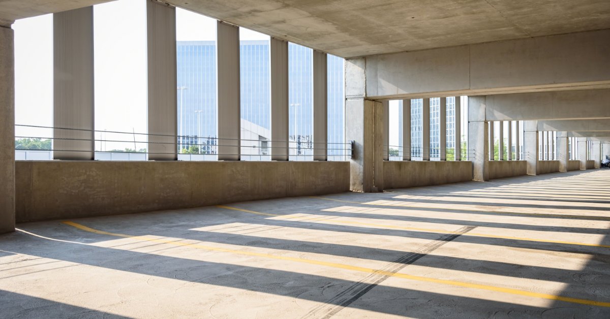 Bright sunlight shining directly into a parking garage next to a skyscraper. The parking garage is empty.