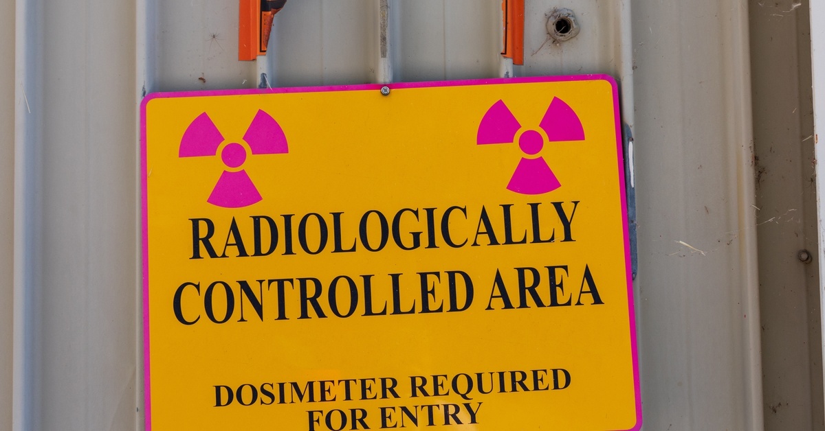 A yellow warning sign with pink radiation symbols reads: RADIOLOGICALLY CONTROLLED AREA, DOSIMETER REQUIRED FOR ENTRY.