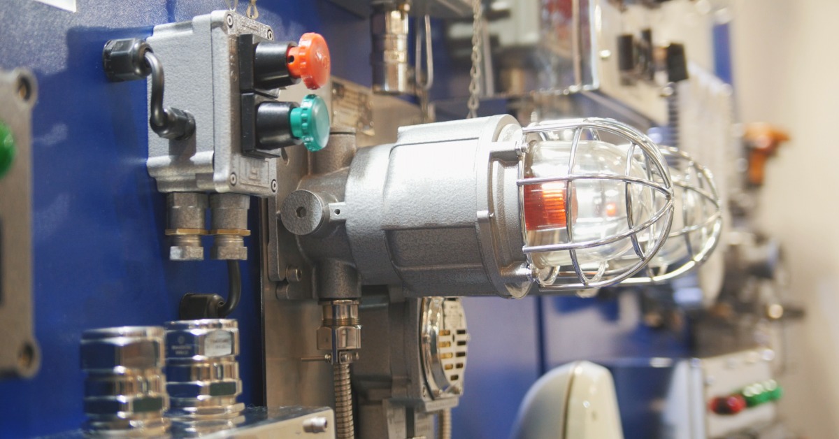 An industrial gas leak control panel and a fire alarm with a protective cage light and control buttons in a work setting.