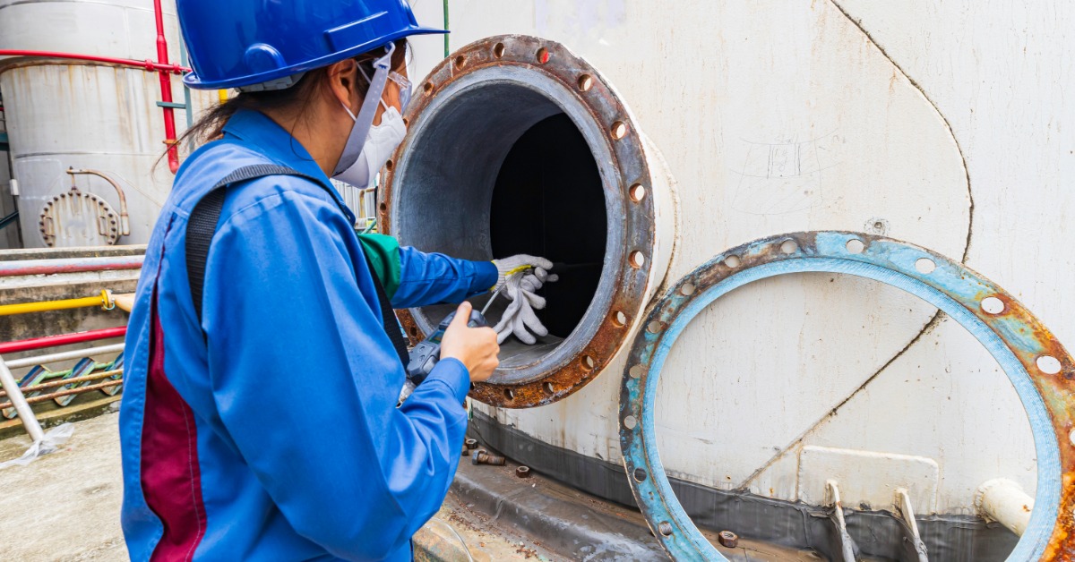 A technician uses a gas monitor to test the air quality inside an industrial storage tank during an inspection.