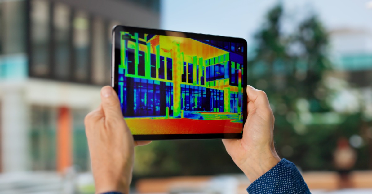 A technician uses a tablet to view a thermal infrared imaging scan of a commercial building exterior.